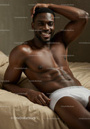 Smiling shirtless man relaxing on beige bedding