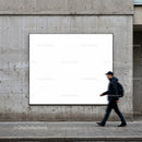 Blurred man walking past large blank billboard on wall