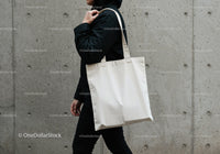 Person carrying plain white tote bag against concrete wall