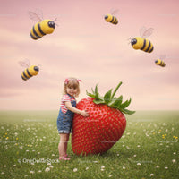 Little girl hugging giant strawberry in flower meadow
