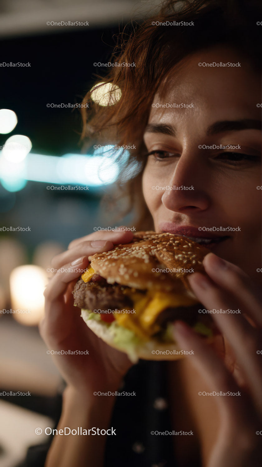 Young woman enjoying a cheeseburger at night in urban setting