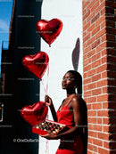 Woman in red dress holding heart balloons and chocolates