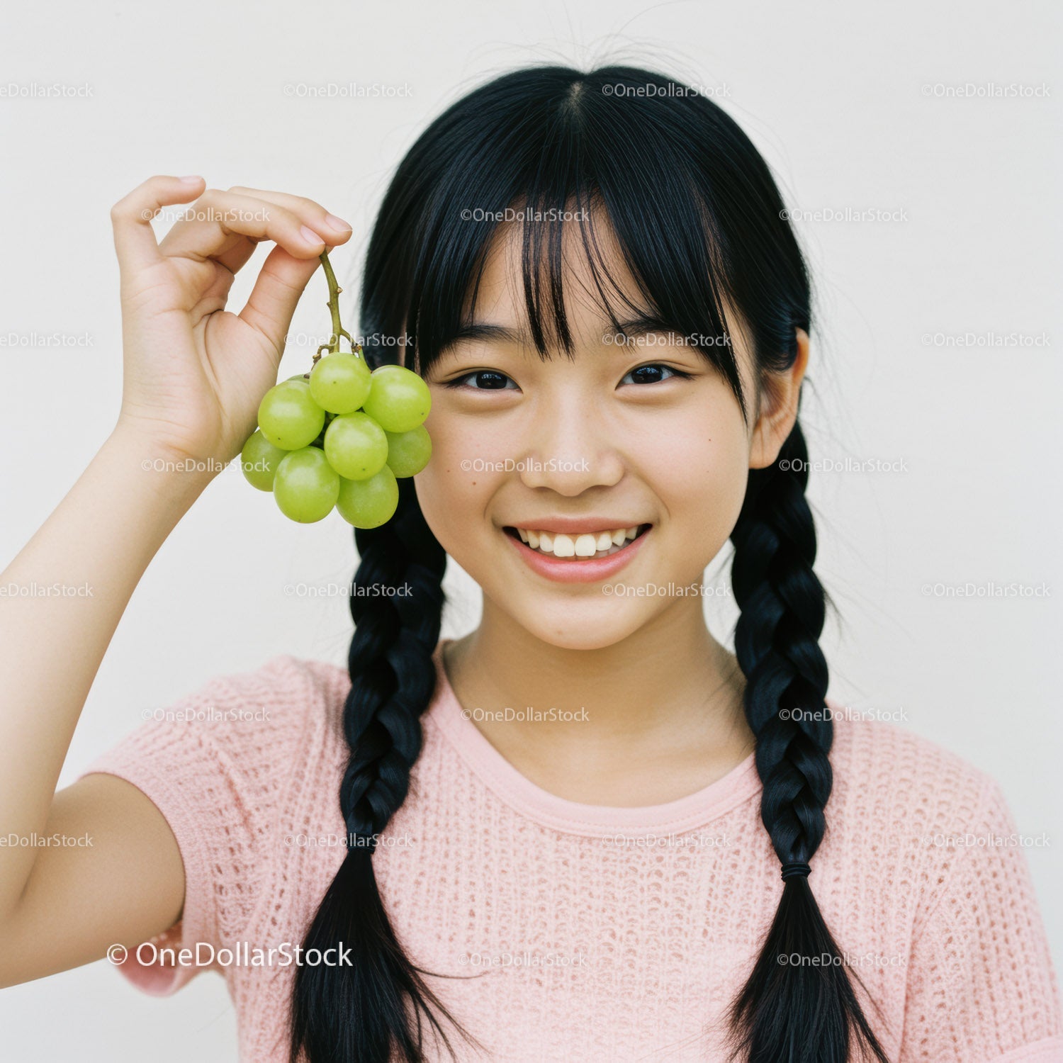 Smiling Girl with Black Braided Hair Holding Green Grapes in Bright Setting