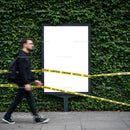 Man walking past caution taped blank billboard outdoors