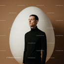 Young man meditating in front of large white egg sculpture