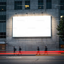 Blurred figures walking past illuminated blank billboard