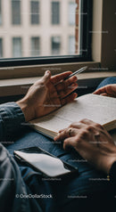 Person Writing in Notebook with Pen Near Window in Indoor Setting