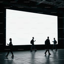Silhouettes of People Walking by Large Illuminated Screen