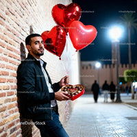 Man holding heart balloons and chocolates at night