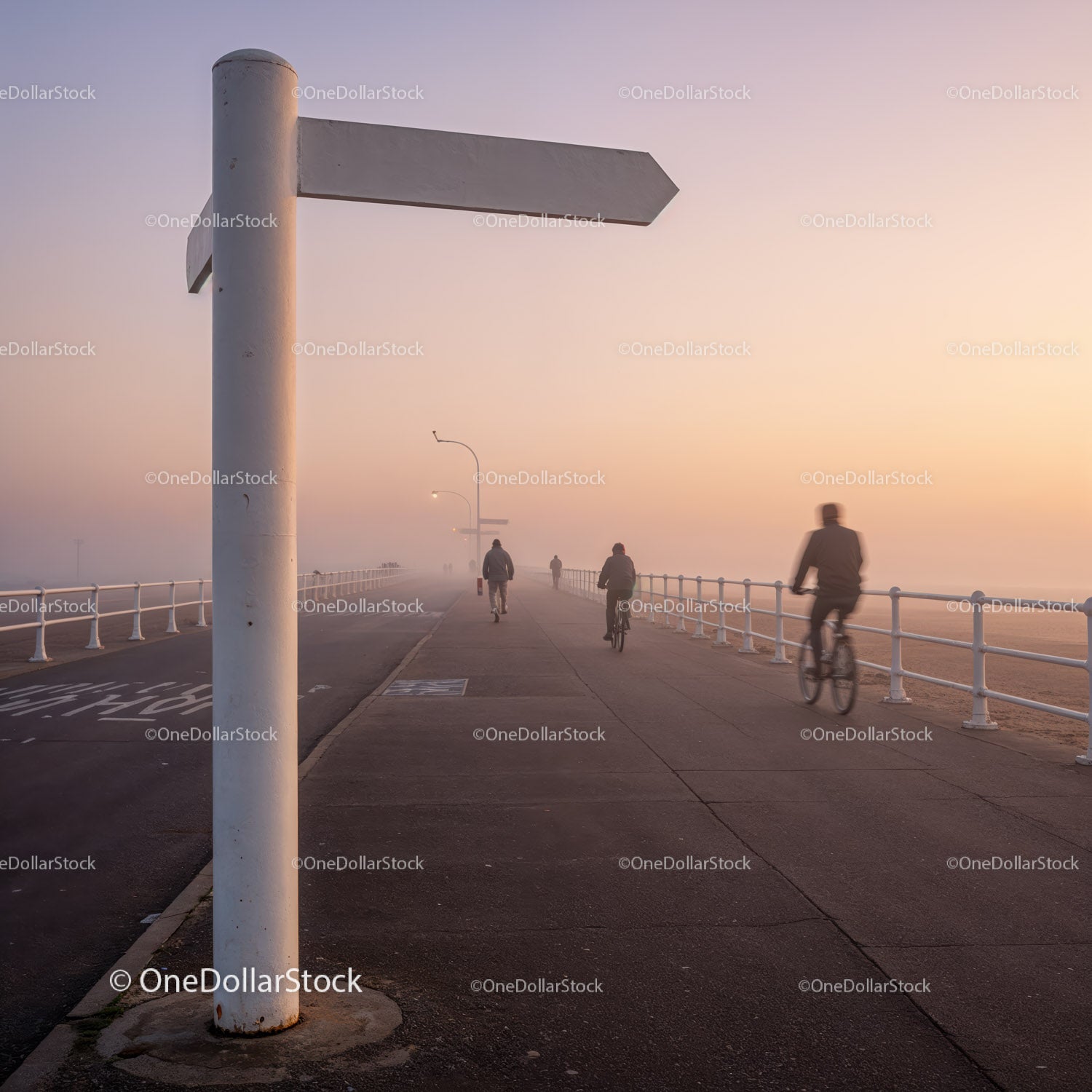 Cyclists and pedestrians on foggy pier at sunrise