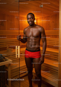 Young shirtless man standing inside a sauna in wooden interior