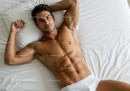 Relaxed muscular man lying on white bed sheets
