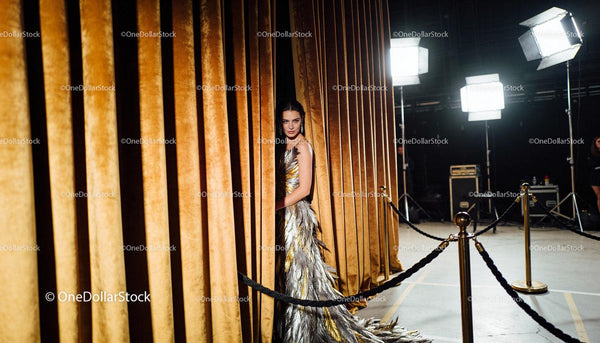 Elegant model emerging from golden velvet curtains
