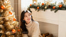 Smiling woman in cozy sweater near golden Christmas tree