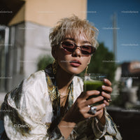 Young Woman with Blonde Curly Hair Wearing Fashionable Sunglasses Holding Green Juice