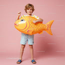 Smiling boy holding large inflatable fish on pink background