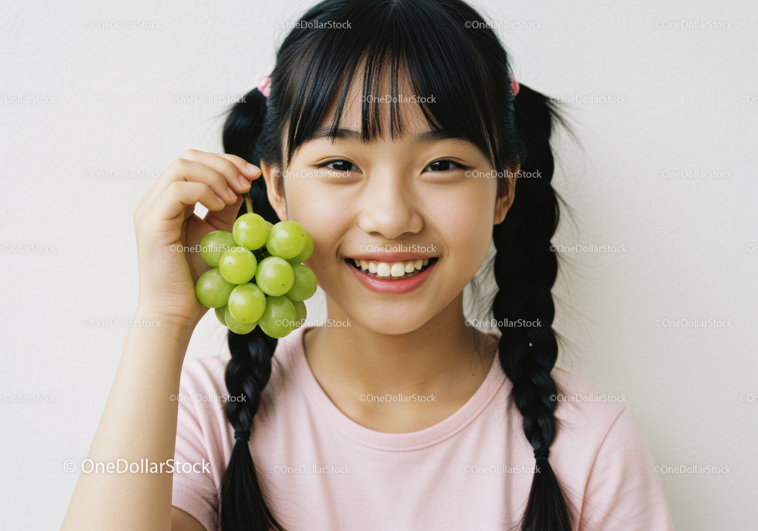 Joyful Girl Smiling with Green Grapes in a Bright Indoor Setting