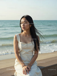 Elegant Woman in White Dress Sitting by Relaxing Seaside Landscape