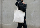 Person carrying plain white tote bag against concrete wall