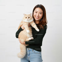 Smiling woman holding fluffy cream cat indoors