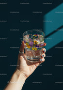 Hand Holding Glass of Floral Infused Water with Ice Cubes