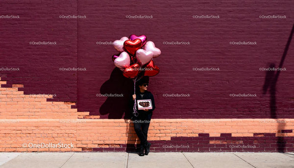 Man Holding Heart Balloons and Chocolates by Brick Wall