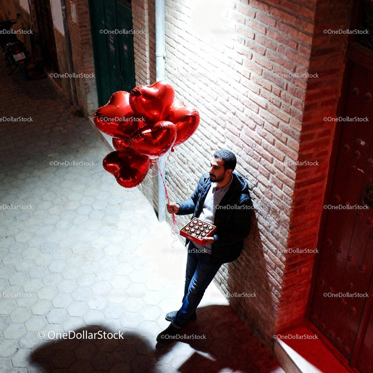 Man standing in alley holding heart balloons and chocolates