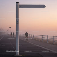 Cyclists Riding Along Misty Seaside Promenade at Dawn