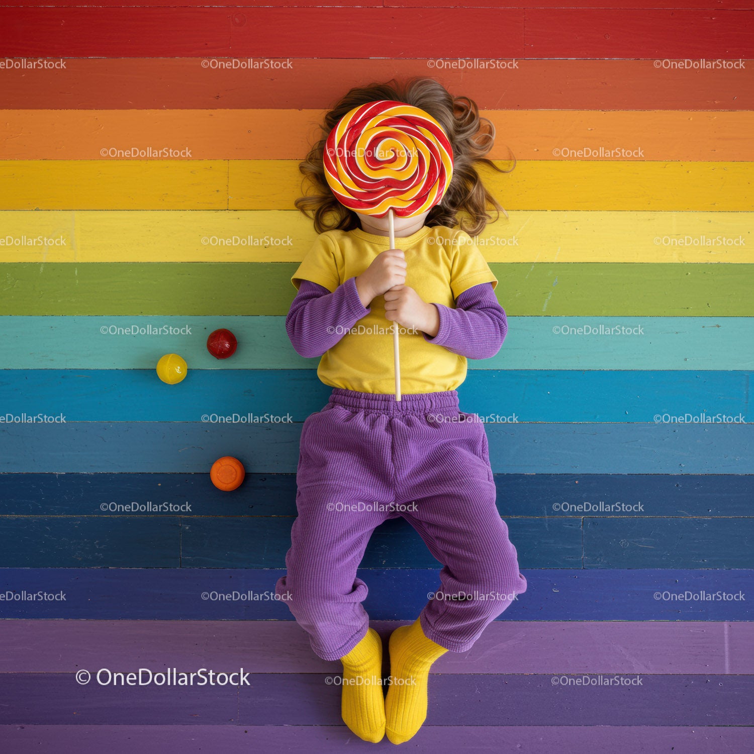 Child lying on colorful rainbow wooden floor with lollipop