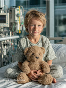Child in Hospital Room Holding Teddy Bear with Medical Equipment Background