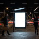 Illuminated urban bus stop billboard at night with pedestrians