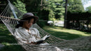 Young Woman Relaxing in Hammock Reading Book in Green Garden