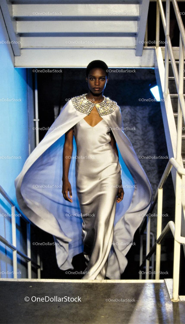 Elegant model in flowing silver gown walking down stairs