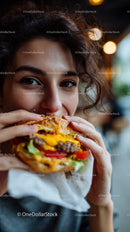 Happy Young Woman Eating Juicy Cheeseburger in Urban Cafe