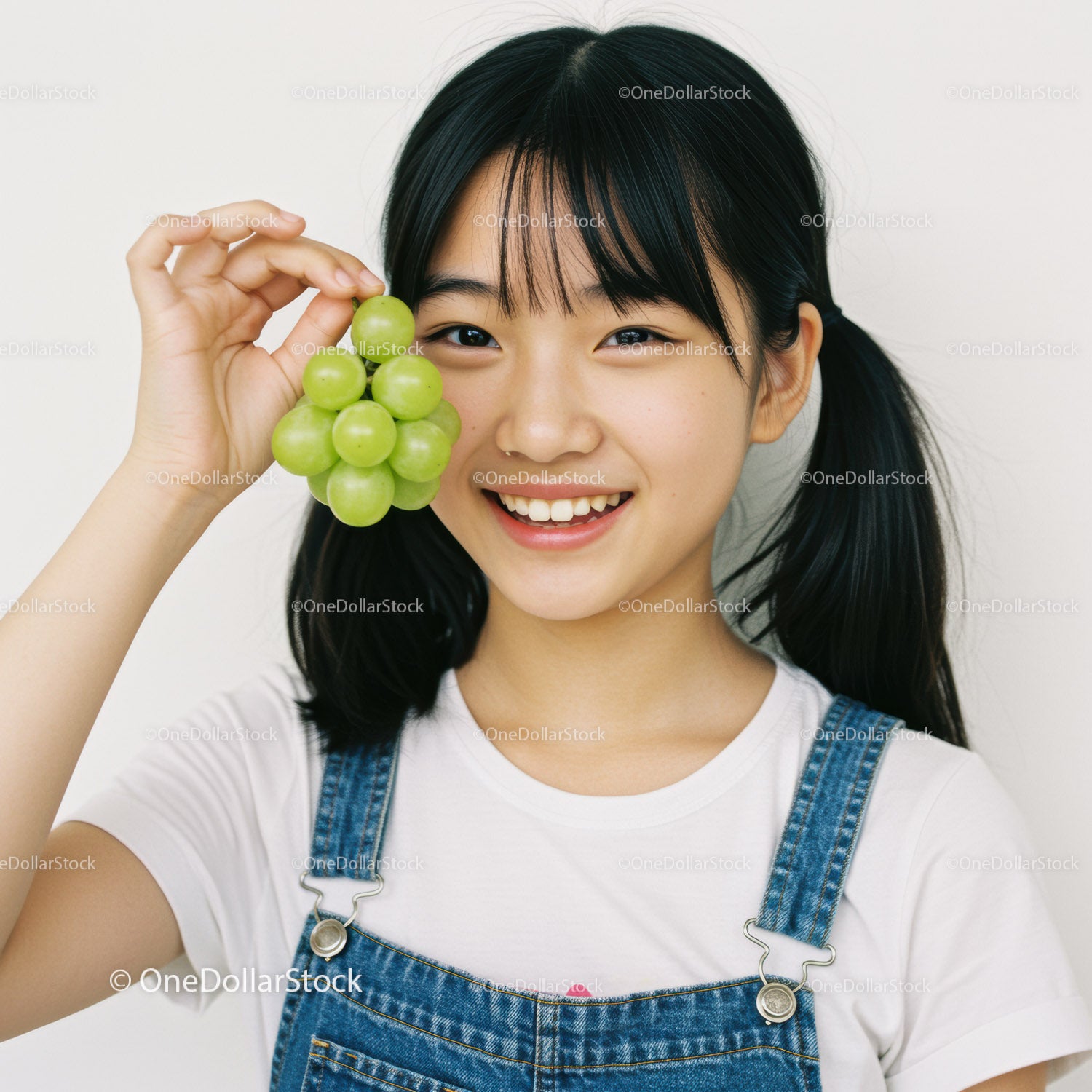 Young Girl Smiling While Holding Bunch of Green Grapes in Casual Outfit