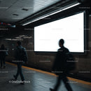 People walking past illuminated blank billboard in subway