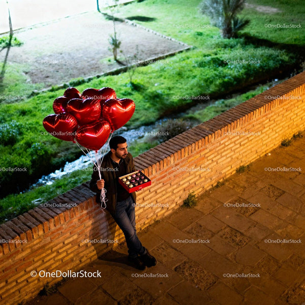 Man Holding Heart Balloons and Chocolates on Walkway