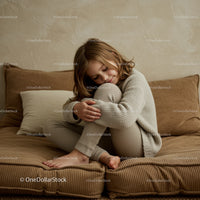 Cozy child hugging knees on soft textured sofa