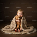 Toddler wrapped in chunky knit blanket hugging teddy bear