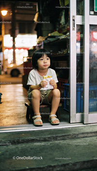 Young child enjoying a sandwich on street at night