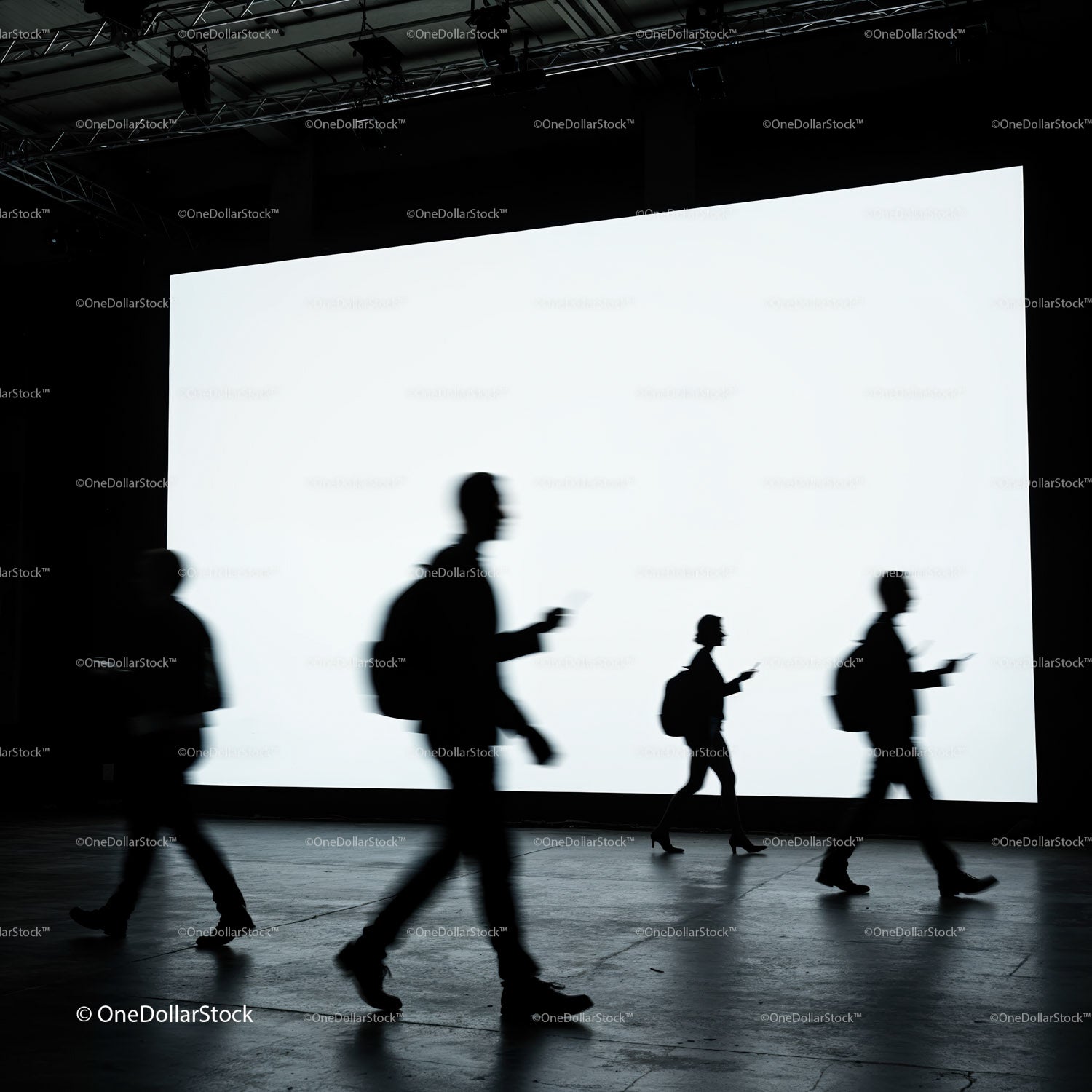 Silhouettes of people walking past bright digital screen