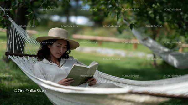 Woman Relaxing in a Hammock Reading a Book in Green Outdoors