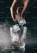 Hand dropping ice cubes into clear glass with splash