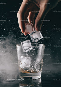 Hand dropping ice cubes into clear glass with splash