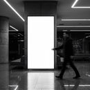 Blurred man walking past illuminated blank billboard indoors