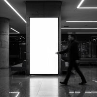 Blurred man walking past illuminated blank billboard indoors