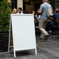 Blank White Sidewalk Sign Outside Busy Café