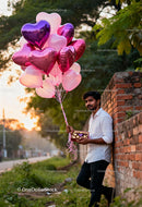 Man holding heart-shaped balloons and chocolates outdoors