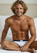 Smiling shirtless man relaxing on bed in white underwear