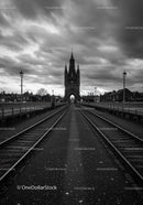 Historic Gothic tower framed by rail tracks and cloudy sky